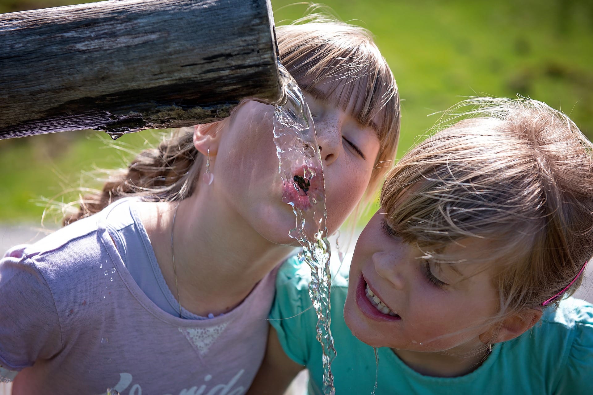 Two white children drinking from a fountain.