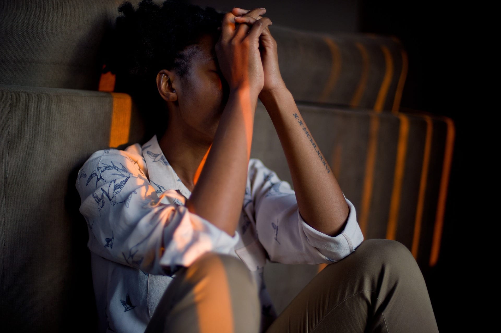 A young, dark-skinned person sitting and hiding their face, stressed.